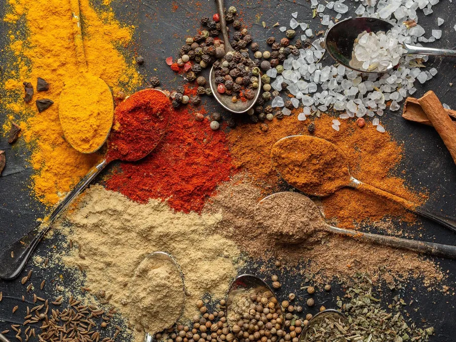 Verschiedene Gewürze auf Löffeln, darunter Kurkuma, Paprika und Pfefferkörner